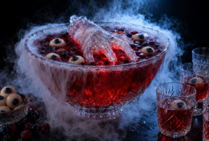 Red punch in a cut-glass bowl with a frozen ice hand and lychee eyeballs, surrounded by fog, next to filled glasses